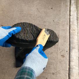 Gloved hands using metal brush to clean boots