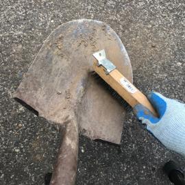 Gloved hand with wire brush cleaning dirt off of shovel