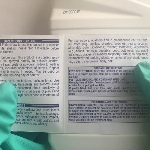 Gloved hands holding pesticide package to read label