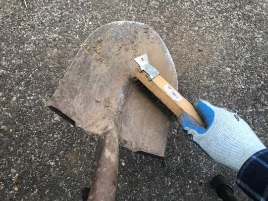 Gloved hand using metal brush to clean shovel