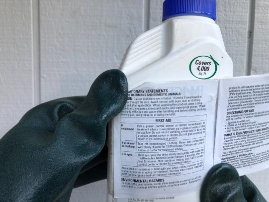 Gloved hands holding herbicide package to read label
