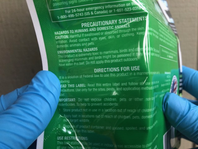 Gloved hands holding rodenticide package to read label